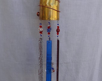 May include: A gold wind chime with a spoon, glass beads, and glass panels hanging from a brass goblet. The beads are red, blue, and white.