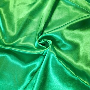 May include: A vibrant, bright green fabric with a smooth, lustrous, and reflective satin finish. The material is gathered in the centre, creating soft, flowing folds and deep shadows that highlight the sheen and texture of the textile surface.