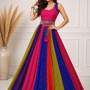 May include: A sleeveless floor-length dress featuring a vibrant, multi-coloured skirt with vertical panels in purple, blue, red, and olive green, all patterned with small white dots. The bodice is bright pink, accented by a wide, embellished waistband.