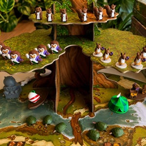 May include: A multi-level cardboard tree structure featuring small brown squirrel figurines on the top branches and various animal figures on the lower levels. The base includes a printed game board with green terrain, a green tent, and small green turtle tokens.