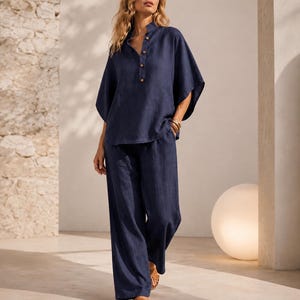 Peut inclure: Un ensemble deux pièces bleu marine foncé composé d'un haut ample à manches courtes avec un col officier et quatre boutons sur le devant, assorti d'un pantalon large. La tenue est confectionnée dans un tissu texturé au tissage visible.