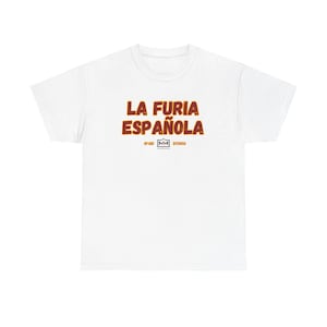May include: A white short-sleeved t-shirt featuring the text LA FURIA ESPAÑOLA in bold, dark orange letters with a thin black outline. Below the text is a small logo with the letters MM inside a rectangle, flanked by the words SPAIN and DUCADOS.