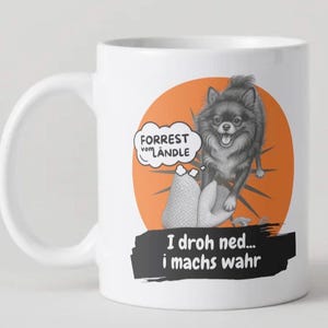 Könnte beinhalten: Weiße Keramik-Tasse mit einer Cartoon-Illustration eines Hundes und dem Text "FORREST vom LÄNDLE" in einer Sprechblase. Unter dem Hund befindet sich der Text "I droh ned... i machs wahr" auf einem schwarzen Banner.