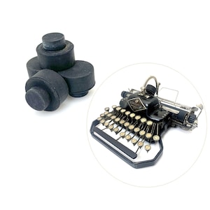 May include: A black vintage typewriter with a black metal frame and a row of keys. The typewriter is sitting on a white surface. There are three black rubber typewriter feet in the background.