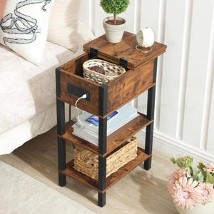 May include: A narrow end table with a dark wood grain finish and black metal frame. It features a hinged top lid revealing a storage compartment, a built-in power outlet with a white charging cable, and two open shelves holding a woven basket.