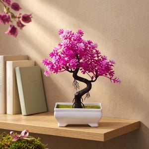 Op de afbeelding: Een miniatuur bonsai boom met felroze bloemen en een donkere, gedraaide stam. De boom staat in een witte rechthoekige pot gevuld met groen mos. De bonsai wordt tentoongesteld op een houten plank, wat een decoratieve en natuurlijke esthetiek creëert.