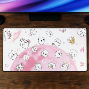 Può includere: Un tappetino da scrivania rettangolare con sfondo bianco e una grande forma circolare rosa al centro. La superficie è decorata con numerosi piccoli personaggi bianchi in stile cartone animato, stelle rosa e piccoli fiocchi rosa sparsi.