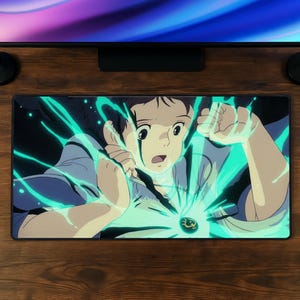May include: A rectangular desk mat featuring a vibrant anime-style illustration of a character with dark hair and wide eyes, surrounded by glowing teal energy emanating from a dark pendant worn around the neck against a dark background.