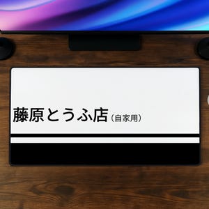 Könnte beinhalten: Eine rechteckige Schreibtischunterlage mit einem weißen oberen Bereich, der den schwarzen japanischen Text 藤原とうふ店 (自家用) enthält, und einem einfarbig schwarzen unteren Bereich, die durch eine dünne weiße horizontale Linie getrennt sind.