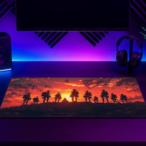 Puede incluir: Una alfombrilla de escritorio rectangular con una vibrante ilustración de atardecer de un grupo de figuras silueteadas de pie sobre una cresta rocosa. La escena muestra un cielo rojo y naranja ardiente con nubes oscuras, resaltando los contornos de los personajes.