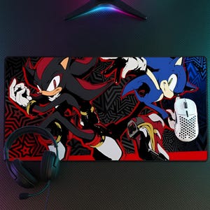 K&ouml;nnte beinhalten: Eine rechteckige Schreibtischunterlage mit einer grafischen Illustration der Charaktere Shadow the Hedgehog und Sonic the Hedgehog vor einem schwarz-roten Musterhintergrund, erg&auml;nzt durch ein schwarzes Headset und eine wei&szlig;e, perforierte Gaming-Maus.