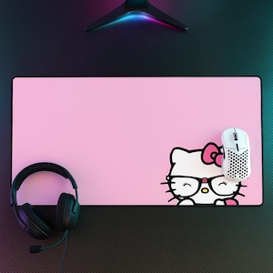 May include: A rectangular light pink desk mat featuring a graphic of a white cat character wearing black glasses and a pink bow. A white honeycomb-patterned computer mouse sits on the right side, and black wired headphones are on the left.