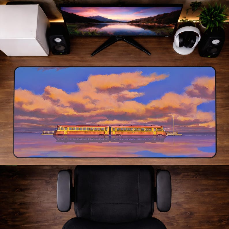 Op de afbeelding: Een rechthoekige bureaumat met een levendige illustratie van een trein op water onder een zonsonderganghemel. De trein is geel en rood, en de lucht is gevuld met oranje en blauwe wolken. De mat is ontworpen voor computergebruik.