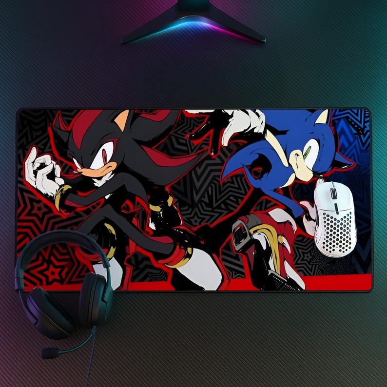 K&ouml;nnte beinhalten: Eine rechteckige Schreibtischunterlage mit einer grafischen Illustration der Charaktere Shadow the Hedgehog und Sonic the Hedgehog vor einem schwarz-roten Musterhintergrund, erg&auml;nzt durch ein schwarzes Headset und eine wei&szlig;e, perforierte Gaming-Maus.