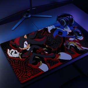 K&ouml;nnte beinhalten: Eine rechteckige Schreibtischunterlage mit einer grafischen Illustration der Charaktere Shadow the Hedgehog und Sonic the Hedgehog vor einem schwarz-roten Musterhintergrund. Eine schwarze Gaming-Maus und schwarze Kopfh&ouml;rer liegen auf der Matte.