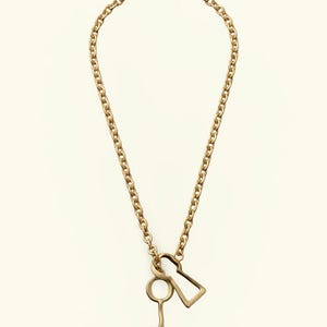 May include: A gold-toned necklace featuring a thick chain link design. Suspended from the chain are two distinct metal pendants: one shaped like a traditional skeleton key and the other shaped like a classic keyhole silhouette, both in gold.