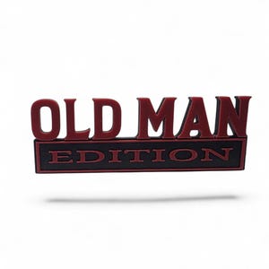 May include: A rectangular patch featuring the text OLD MAN in bold, raised red lettering above a black rectangular border containing the word EDITION in red capital letters. The design has a clean, structured appearance with high contrast.