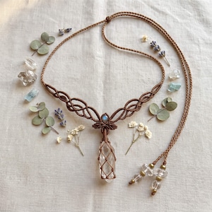 May include: A brown macrame necklace featuring a central clear quartz crystal point encased in a woven cord cage, accented with a small iridescent moonstone cabochon, and finished with two clear crystal beads and brass spacers on the cord ends.