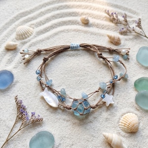 May include: A multi-strand bracelet made of brown cord featuring light blue beads, a central raw blue stone encased in netting, a white mother-of-pearl fish charm, and a white mother-of-pearl star charm, finished with adjustable sliding knots.