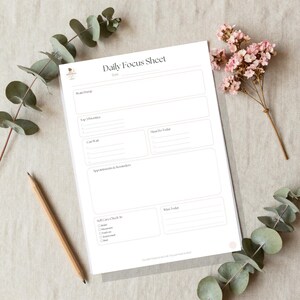 Op de afbeelding: Een wit Daily Focus Sheet plannerblad met secties voor datum, brain dump, top 3 priorities, must do today, can wait, appointments and reminders, self care check in en wins today, vergezeld van een houten potlood en eucalyptus.