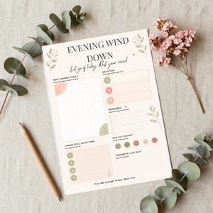 Op de afbeelding: Een geprint "Evening Wind Down" plannerblad met secties voor dankbaarheid, herinneringen en gevoelens. De pagina bevat tekst waaronder "EVENING WIND DOWN" en "Let go of today. Rest your mind." versierd met illustraties van groene bladeren.