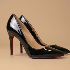 Puede incluir: Un par de zapatos de tac&oacute;n alto de charol negro con punta afilada y tac&oacute;n de aguja fino. Los zapatos presentan un acabado liso y brillante y una suela roja distintiva visible en la parte inferior y en la parte posterior del tac&oacute;n.