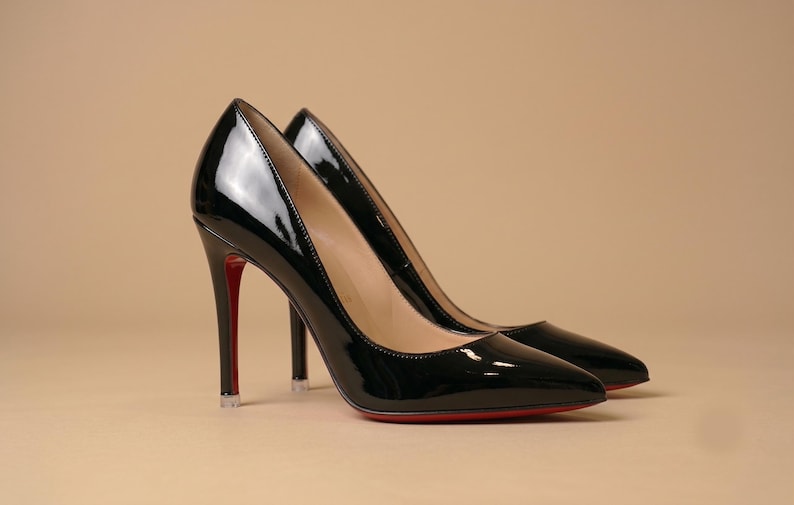 Puede incluir: Un par de zapatos de tac&oacute;n alto de charol negro con punta afilada y tac&oacute;n de aguja fino. Los zapatos presentan un acabado liso y brillante y una suela roja distintiva visible en la parte inferior y en la parte posterior del tac&oacute;n.