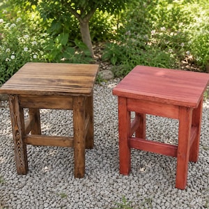 May include: Two square wooden stools with four legs and horizontal support bars. One stool features a dark brown wood grain finish, while the other stool is finished in a solid red color. Both stools have a flat top surface and a sturdy frame.