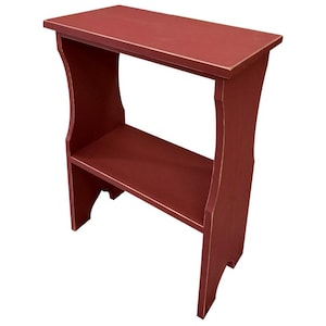 Pode incluir: Uma pequena mesa lateral retangular de madeira pintada em um tom de vermelho profundo com um acabamento desgastado nas bordas. A mesa possui uma superf&iacute;cie superior plana, uma prateleira inferior &uacute;nica e dois pain&eacute;is laterais verticais com recortes.