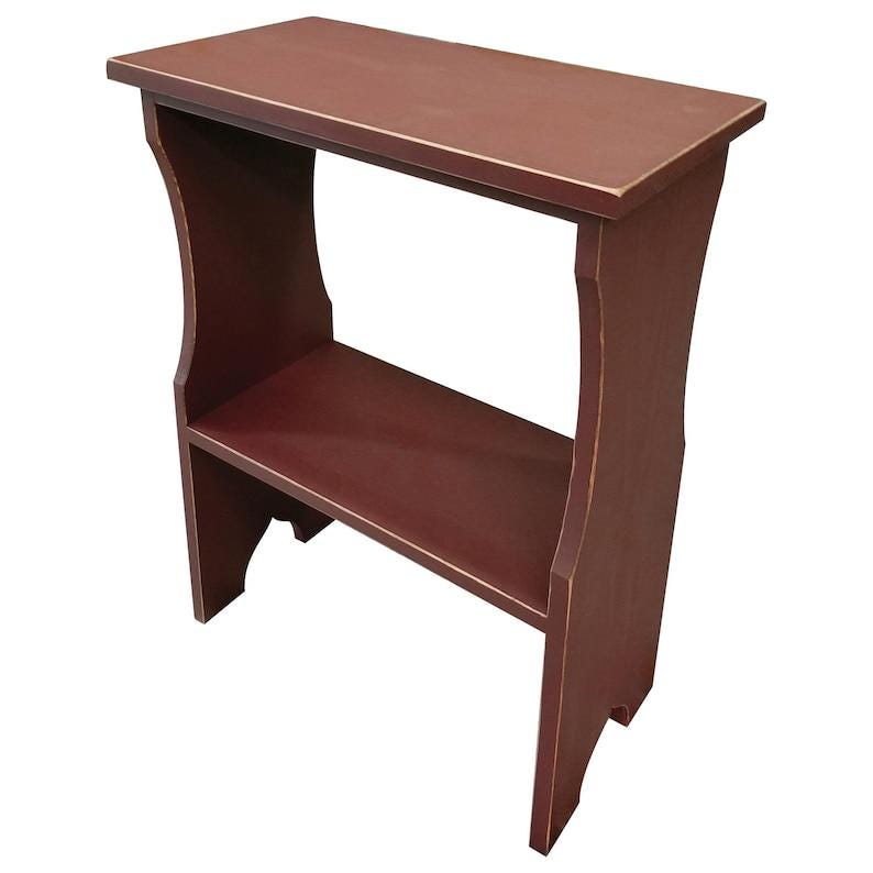 Pode incluir: Uma mesa lateral de madeira em vermelho escuro com uma superf&iacute;cie superior retangular e uma prateleira inferior &uacute;nica. A mesa possui dois pain&eacute;is laterais verticais com recortes curvos e um acabamento desgastado nas bordas.