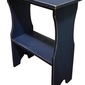 Pode incluir: Uma mesa lateral de madeira azul-marinho com um tampo retangular e uma prateleira inferior &uacute;nica. A pe&ccedil;a apresenta pain&eacute;is laterais curvos e bordas de madeira clara vis&iacute;veis nos cantos, proporcionando um acabamento desgastado &agrave; pintura azul.