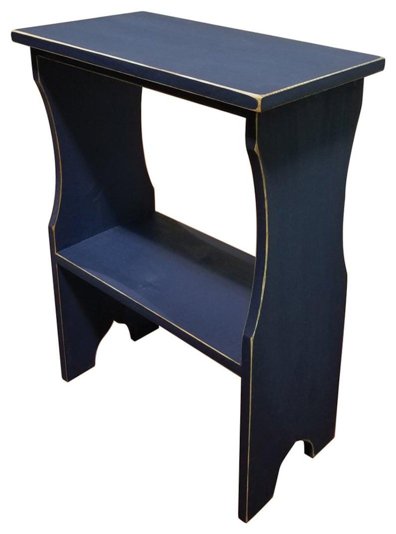 Pode incluir: Uma mesa lateral de madeira azul-marinho com um tampo retangular e uma prateleira inferior &uacute;nica. A pe&ccedil;a apresenta pain&eacute;is laterais curvos e bordas de madeira clara vis&iacute;veis nos cantos, proporcionando um acabamento desgastado &agrave; pintura azul.