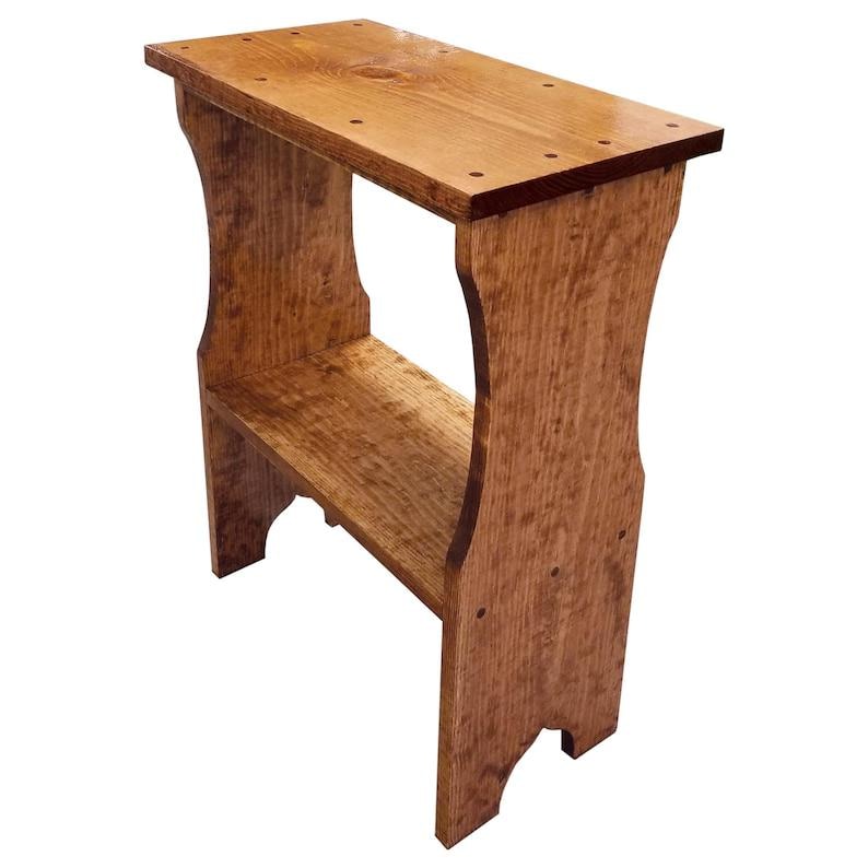 Pode incluir: Uma mesa lateral retangular de madeira com acabamento castanho m&eacute;dio e veios de madeira vis&iacute;veis. A mesa apresenta uma superf&iacute;cie superior plana com seis pequenas reentr&acirc;ncias circulares, uma prateleira inferior e dois pain&eacute;is laterais curvos.