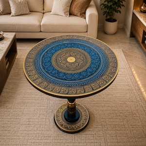 May include: A round pedestal table featuring a vibrant blue and gold hand-painted mandala design on the tabletop. The central motif is surrounded by intricate floral patterns and a decorative border. The base is also painted with matching gold details.