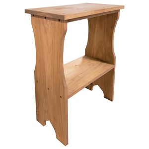 Pode incluir: Uma mesa lateral de madeira castanho-claro com uma superf&iacute;cie superior retangular e uma prateleira inferior. A estrutura &eacute; suportada por dois pain&eacute;is laterais verticais com recortes curvos na base e detalhes de uni&atilde;o circulares vis&iacute;veis.