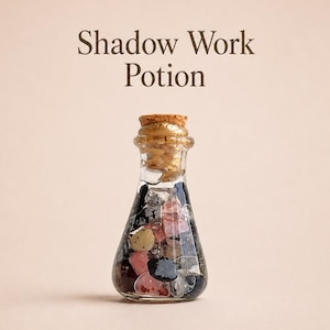 May include: A small, clear glass bottle with a cork stopper, filled with a collection of polished stones in shades of black, pink, and white. The text 'Shadow Work Potion' is printed in dark brown letters above the bottle.