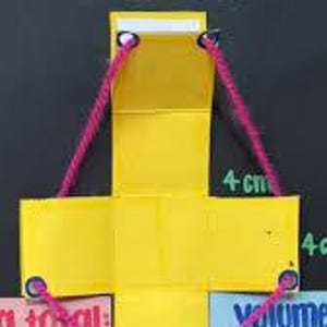 May include: A yellow paper cross-shaped net of a cube on a black background with the word CUBO at the top. Pink yarn connects the corners of the yellow paper. Text on the right indicates 4 cm measurements and volume calculations are visible.