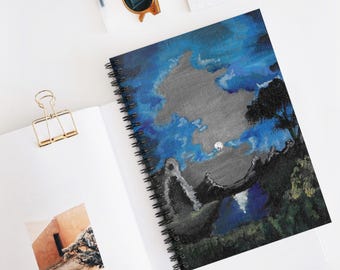 May include: Spiral-bound notebook featuring a landscape painting with a night sky, moon, and trees. The cover art has shades of blue, gray, and black. The notebook is open, revealing a blank page and a small photo.