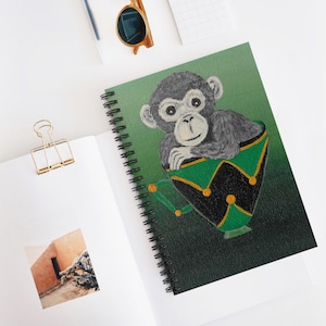 May include: A green, black, and gold cup with a small monkey sitting inside. The monkey is gray and has a white face. The cup has a green rim and a black base with gold accents.