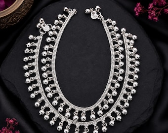 May include: A pair of silver-toned anklets featuring a braided chain design adorned with numerous small, dangling spherical bells along the entire length. Each anklet includes a secure clasp mechanism at the ends, showcasing a polished metallic finish.