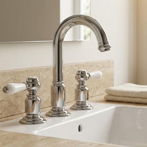 May include: A polished chrome bathroom faucet featuring a high-arc spout and two separate handles with white ceramic lever accents. The faucet is mounted on a beige stone countertop next to a white sink basin and a folded beige towel.