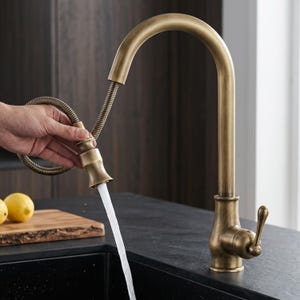 May include: A high-arc kitchen faucet with an antique brass finish, featuring a pull-down sprayer head attached to a flexible coiled hose. The faucet has a single side-mounted lever handle and is shown dispensing a steady stream of water.