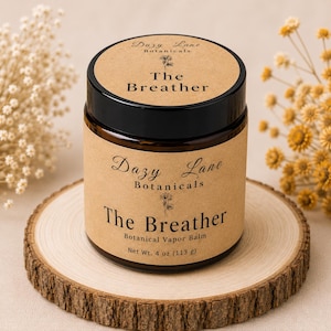 May include: A cylindrical amber glass jar with a black lid, featuring a tan paper label printed with Dazy Lane Botanicals, The Breather, and Botanical Vapor Balm. The label clearly states a net weight of 4 oz (113 g) on the front surface.