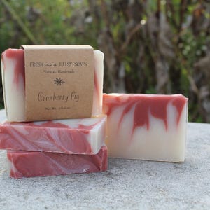 May include: Four bars of handmade soap stacked on top of each other. The top bar has a brown label that reads "Fresh as a Daisy Soaps, Natural Handmade, Cranberry Fig, Net Wt. 3.5 oz."