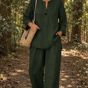 May include: A dark green long-sleeved shirt with a single button closure and a matching pair of wide-leg trousers. The shirt features a split neckline and the trousers include side pockets. A woven straw shoulder bag is carried alongside the outfit.