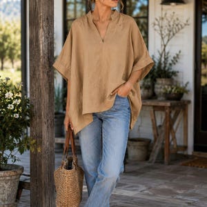 May include: A tan V-neck tunic with short, wide sleeves and a loose fit, paired with light blue denim jeans, white sneakers, and a woven straw tote bag. The tunic features a simple collarless neckline and cuffed sleeves, creating a relaxed look.