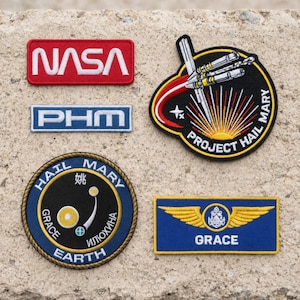 May include: Four embroidered patches featuring space-themed designs. One red NASA rectangle, one blue PHM rectangle, one circular Project Hail Mary patch with a rocket, and one circular Hail Mary Earth patch with a blue and yellow wing badge.