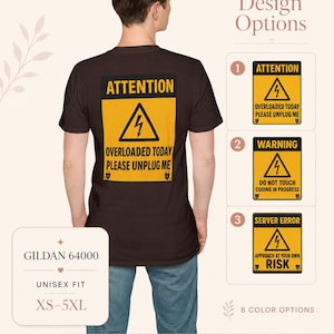 Puede incluir: Una camiseta de color marrón oscuro con un gráfico amarillo y negro en la parte posterior que se asemeja a una señal de peligro. El gráfico incluye un icono de rayo y el texto ATTENTION OVERLOADED TODAY PLEASE UNPLUG ME. Se muestran tres opciones de diseño adicionales.