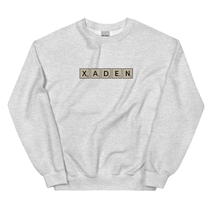 May include: A gray sweatshirt with the name "XADEN" spelled out in black letters on beige tiles.