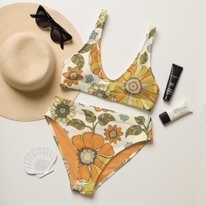 May include: A white and orange floral print bikini with a high-waisted bottom. The bikini is laid out on a white surface with a straw hat, sunscreen, and a seashell.